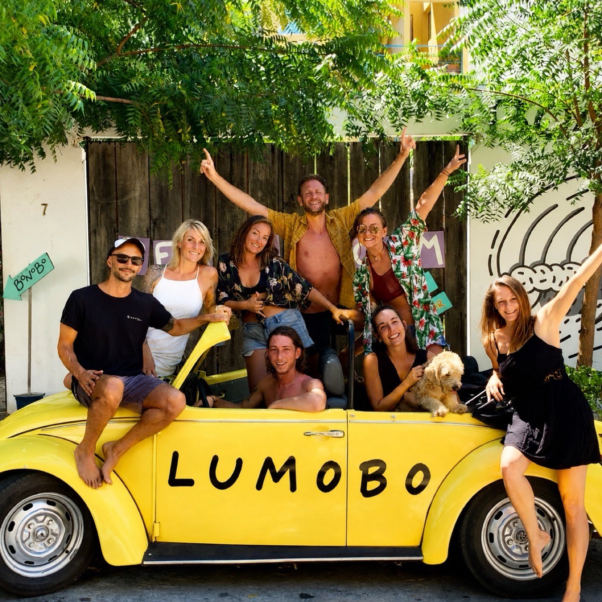 A yellow VW Beetle painted LUMOBO, packed with laughing friends